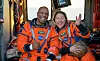 Two astronauts in bright orange NASA flight suits smiling inside a Navy rescue helicopter.