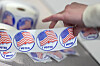 Hand picking an I Voted sticker from a roll with U.S. flag design.