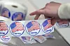 Hand picking an I Voted sticker from a roll with U.S. flag design.