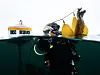A diver in scuba gear works below the water surface beside yellow buoys and a small research float.