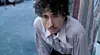 Bob Dylan i lys skjorte foran en blå væg.
