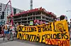 Des manifestants marchent dans la rue à Montréal avec une grande bannière jaune et des drapeaux rouges.