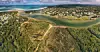 Aerial coastal landscape with an inlet, seaside homes, beaches and forested dunes.