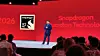 Presenter on a red-lit stage beside a Snapdragon Guardian Technology display, facing an audience.