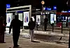 Personer ved en opplyst kollektivholdeplass på kveldstid.