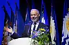 Unidentified speaker at a podium with flowers and flags in the background
