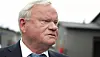 John Fredriksen, de cabello canoso y traje, observa el entorno frente a un edificio.