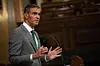 Pedro Sánchez Pérez-Castejón, con traje gris y corbata verde, gesticula ante un estrado en una sala institucional.