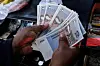 Manos cuentan varios billetes de 10 ZiG junto a una caja registradora.
