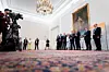 Austrian officials stand in a grand room during a press conference as photographers film from the left.