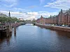 A canal in Hamburg, Germany, bordered by historic red-brick buildings under a bright blue sky.