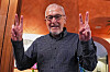 Francis Halzen smiles and raises both hands in a hotel in Turin, making victory signs after his Nobel Prize win.