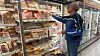 Persona con chaqueta azul revisa alimentos en vitrinas refrigeradas de un supermercado.