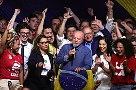 Lula sostiene un micrófono y una bandera de Brasil mientras celebra rodeado de simpatizantes.