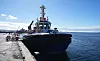 Remolcador negro atracado en un muelle de Punta Arenas, con mar abierto y cielo despejado al fondo.