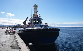 Remolcador negro atracado en un muelle de Punta Arenas, con mar abierto y cielo despejado al fondo.